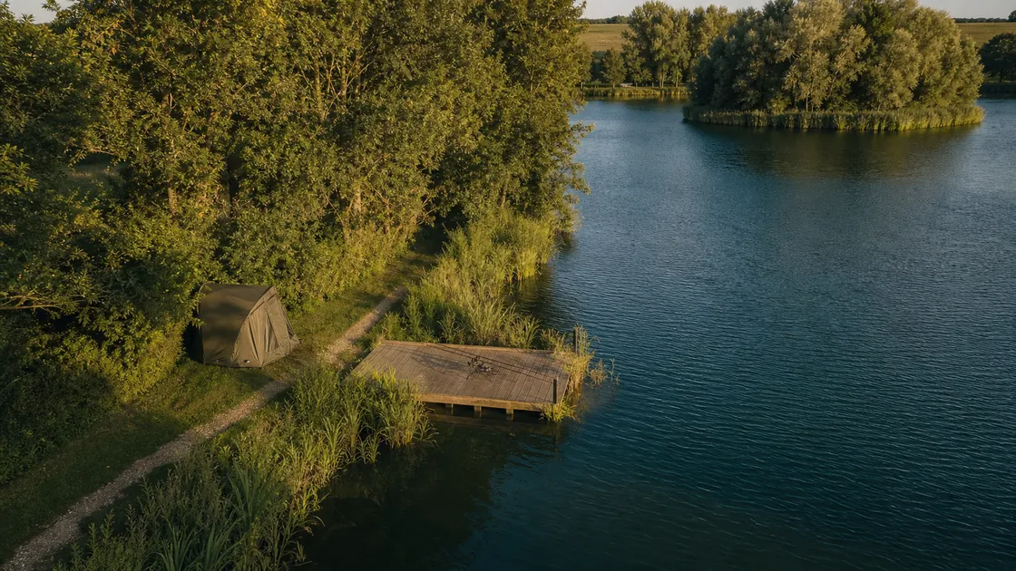 A bivvy and wooden platform swim on the tree-lined bank of Chad Pool, seen from above at golden hour